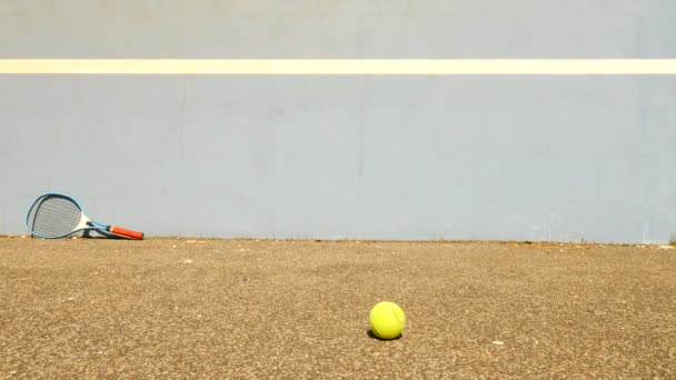 Lege opleiding tennisbaan met blauwe stuiteren tennis muur. Oude gele bal is springen op het slechte asfalt-grond - Video