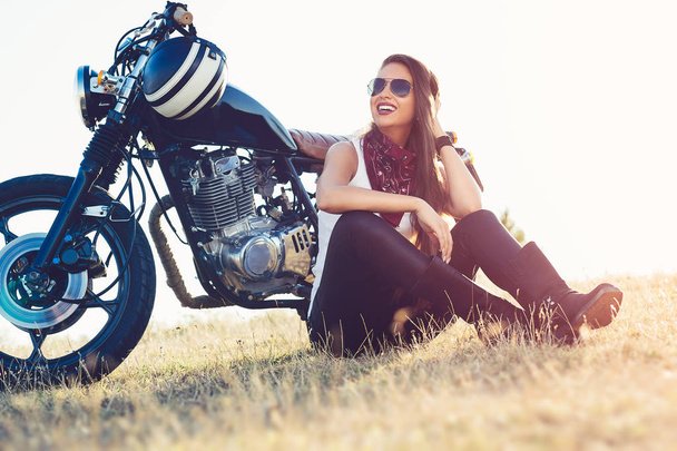 Beautiful biker woman sitting by her motorcycle on a highway. - Foto, Imagem