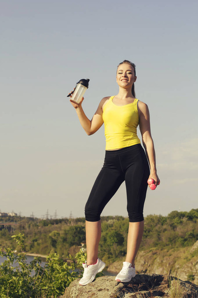 Young beautiful woman doing sport exercises and drinking water outdoors - 写真・画像