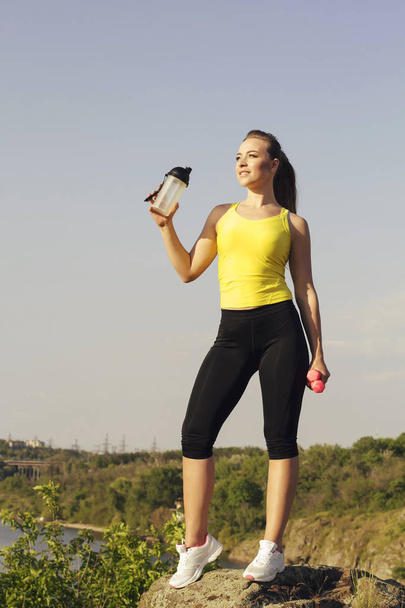 Young beautiful woman doing sport exercises and drinking water outdoors - Foto, Imagen