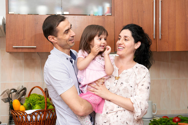 family portrait in kitchen interior with fresh fruits and vegetables, healthy food concept, pregnant woman, man and child girl - Photo, Image