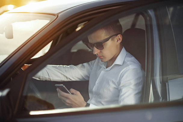 Привабливий красивий чоловік в сонцезахисних окулярах, використовуючи смартфон у своїй машині
 - Фото, зображення