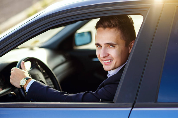 Attractive handsome smiling man in a business suit driving an expensive car - Foto, imagen