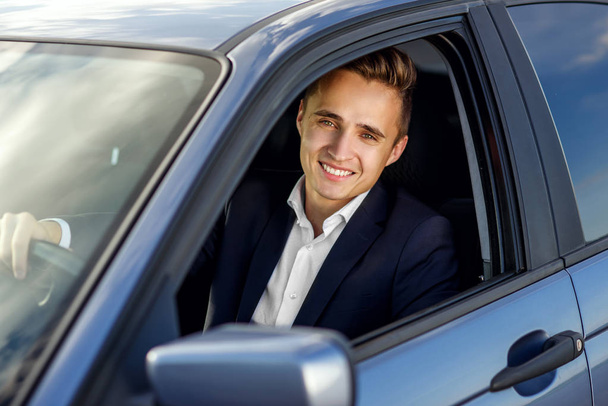Atractivo hombre guapo sonriente en un traje de negocios que conduce un coche caro
 - Foto, Imagen