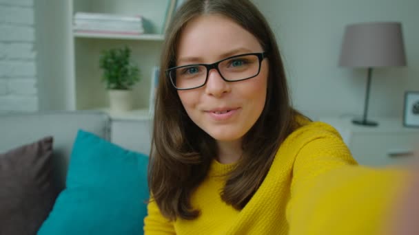 Young beautiful teen girl making video call. Teen girl talking to friends online, video chatting, blogging, waving hand, laughing while sitting on the couch at home. Close up - Materiał filmowy, wideo
