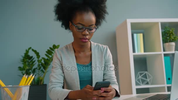 Black african american woman wearing glasses and using smart phone at the office - Кадри, відео