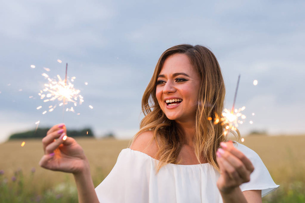 Outdoor photo of young beautiful happy smiling girl holding sparkler. Holidays concept. - Foto, imagen
