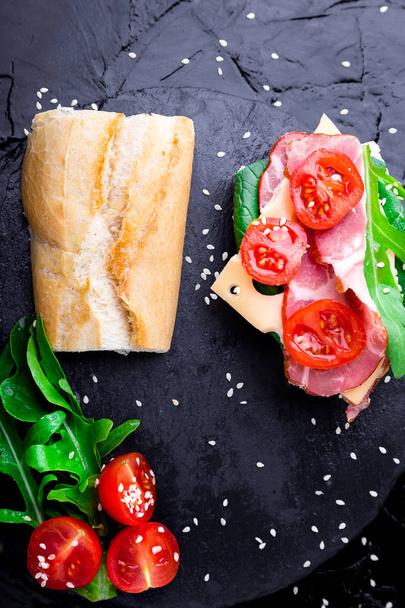 Sandwich ouvert avec confiture, roquette, tomates, fromage sur fond noir d'ardoise de pierre. Vue du dessus
 - Photo, image