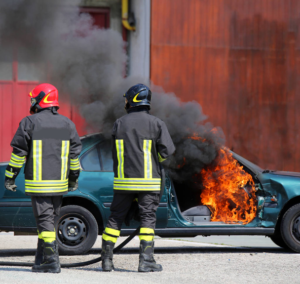 incident car with flames and black smoke and two firefighters - Photo, Image