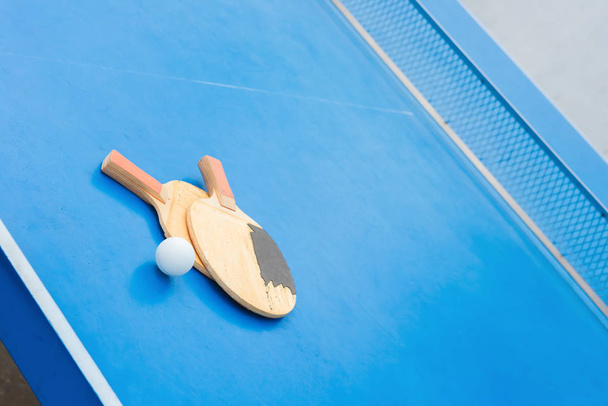 raquetes velhas do pingpong e bola e rede em uma tabela azul do pingpong
 - Foto, Imagem