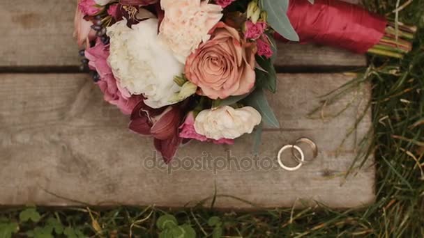 Wedding rings and wedding bouquet at wooden and grass surface - Footage, Video