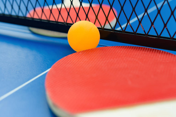 raquetas de pingpong y bola y red en una mesa de pingpong azul de cerca
 - Foto, Imagen