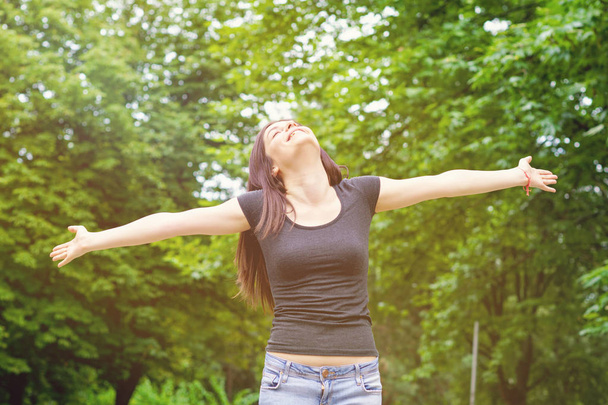 Młoda kobieta w słonecznym parku z wyciągniętymi ramionami - Zdjęcie, obraz