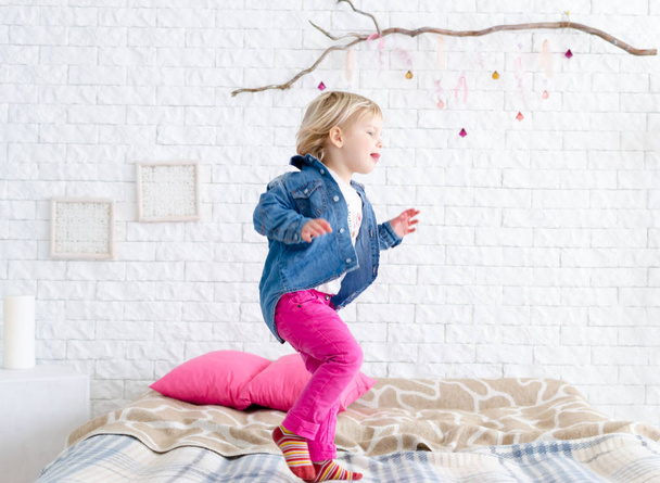 Happy child girl jumps on bed - Foto, afbeelding
