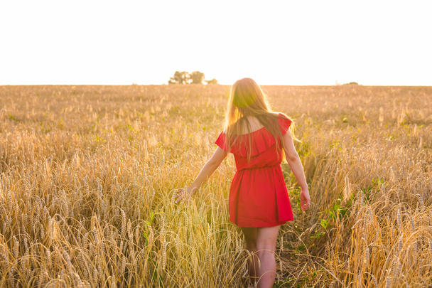 国、自然、夏の休日、休暇、人々 コンセプト - 穀物のフィールドに赤いドレスで幸せな若い女 - 写真・画像