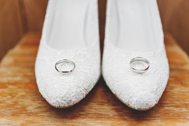 Pair of golden wedding rings on laced bridal shoes. Traditional  - Zdjęcie, obraz