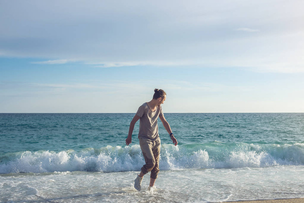 Joven hombre feliz caminando en zapatillas mojadas del mar en la orilla y huyendo de las olas
 - Foto, Imagen