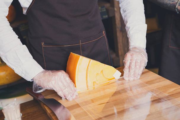 Assistente de loja embrulhando um pedaço de queijo
 - Foto, Imagem