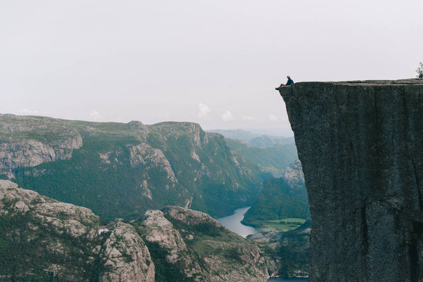 Man sitting on the edge of Preykestalen, Norway - 写真・画像