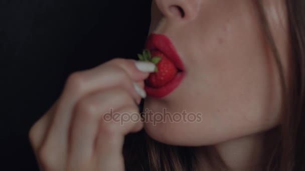 Close-Up Shot: van Sexy jonge meisje met rode lippenstift eten aardbeien die genieten van de smaak op zwarte achtergrond - Video