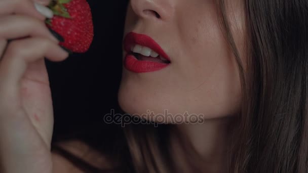 Meisje met rode lippen erotische eet een grote aardbei genieten van de smaak op zwarte achtergrond - Video
