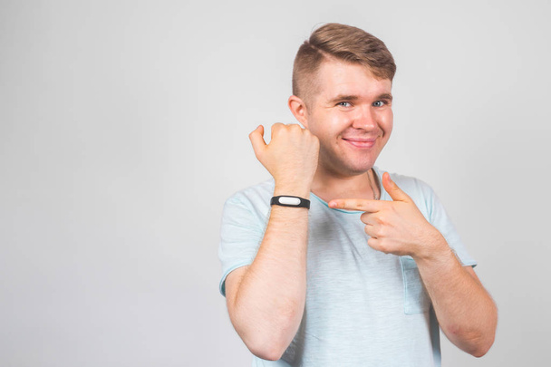 Cheerful young man standing and pointing on fitness tracker over grey background - Photo, Image