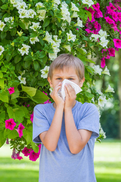 Allergia. Kisfiú fúj az orrát, közel a fa virágzik. - Fotó, kép