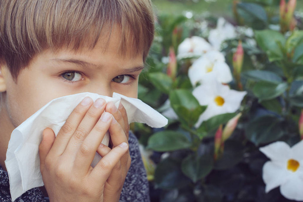 Αλλεργία. Παιδί φυσάει τη μύτη του κοντά σε λουλούδια που ανθίζουν - Φωτογραφία, εικόνα