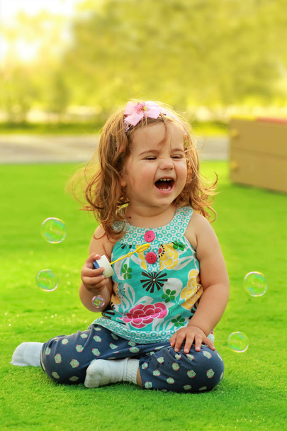 Ridendo una ragazza di un anno che impara a soffiare bolle di sapone e divertirsi sul prato
 - Foto, immagini