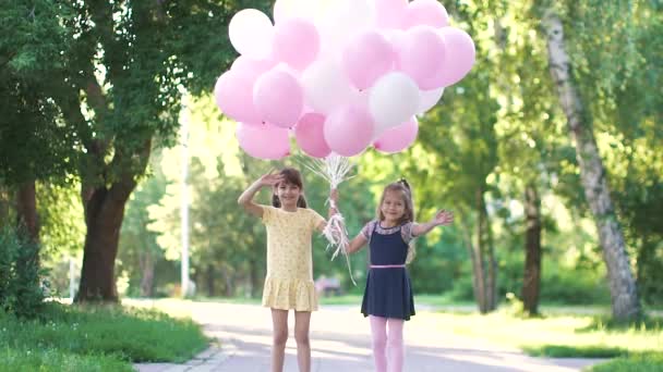 Πορτραίτο των μικρών κοριτσιών με μπαλόνια. δύο μικρές φίλες κρατώντας τα χέρια, χαμογελώντας και εξετάζοντας τη φωτογραφική μηχανή. αργή κίνηση - Πλάνα, βίντεο