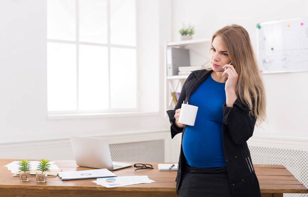 Femme d'affaires enceinte parlant au téléphone avec tasse
 - Photo, image