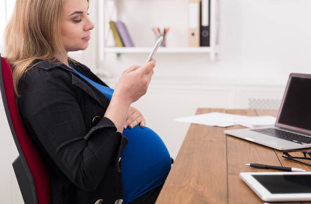Jeune femme enceinte utilisant un smartphone au bureau
 - Photo, image