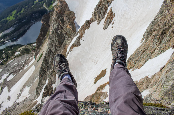 Turysta wisi jego nogi na krawędzi klifu w górach skalistych. - Zdjęcie, obraz