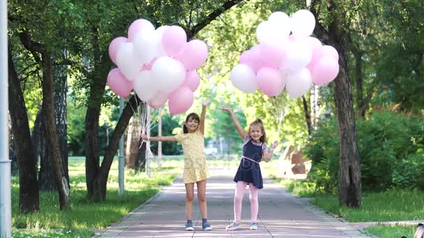 two little girls are holding a lot of balloons, smile and wave hands - Footage, Video
