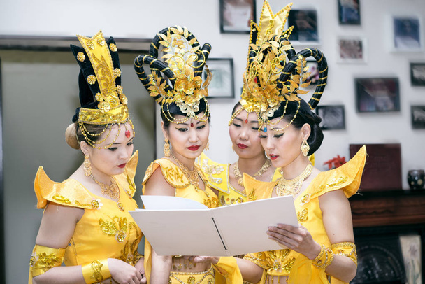 τέσσερις ασιατικές γυναίκες ηθοποιούς σε παραδοσιακό ταϊλανδέζικο κίτρινο κοστούμια ανάγνωση κενό βιβλίο με αντίγραφο χώρο για το κείμενό σας - Φωτογραφία, εικόνα