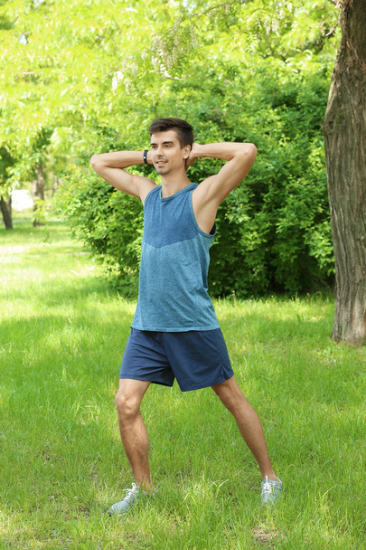 Athletic young man doing bicycle crunch exercise while standing on grass in green spring park - Foto, afbeelding
