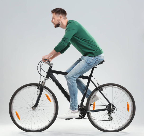 Handsome young man riding bicycle on light background - Фото, зображення