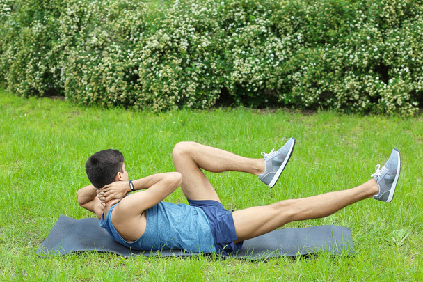 Athletic young man doing bicycle crunch exercise while lying on mat outdoors - Photo, Image