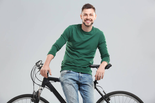 Handsome young man with bicycle on light background - Foto, Bild