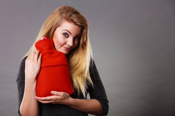 Woman holding warm red hot water bottle - Foto, afbeelding