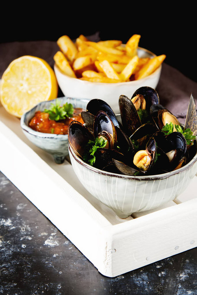 Mussels with herbs in a bowl with lemon and French fries on a wh - Фото, изображение