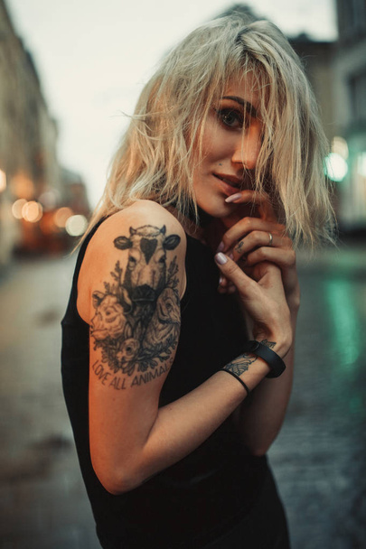 Portret młodej kobiety z tatuażem na ramieniu stojąc na ulicy w godzinach wieczornych. - Zdjęcie, obraz