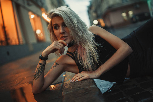 Portrait of young woman lying on wet pavement on city street in  - Photo, Image