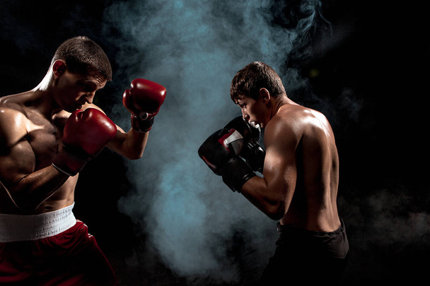 Two professional boxer boxing on black smoky background, - Foto, Imagen