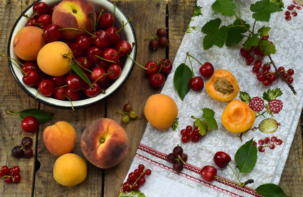 Fresh fruits and berries on wooden background. Ripe sweet cherry, currants, peach and apricot in bowl on the kitchen table. - Foto, Imagem