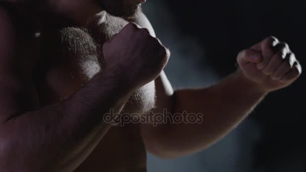 Savaşçı siluet. Yakışıklı atletik adam boks standında karanlık bir arka plan üzerinde. Kas genç adam boks eldivenleri ve şort farklı hareketleri ve grevler gösterir - Video, Çekim