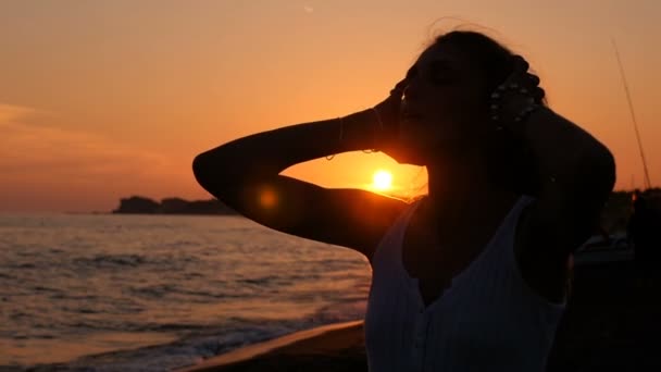 Silhouet van ontspannen vrouw handen haar met haar handen bij zonsondergang op het strand - Video