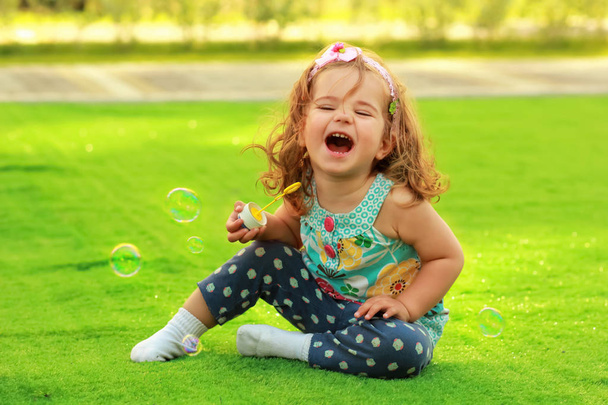 Laughing one year old girl learning to blow soap bubbles and having fun on the lawn - Photo, Image