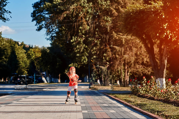 Pretty little girl in red t-shirt learning to roller skate outdoors on beautiful summer day - Foto, Imagem
