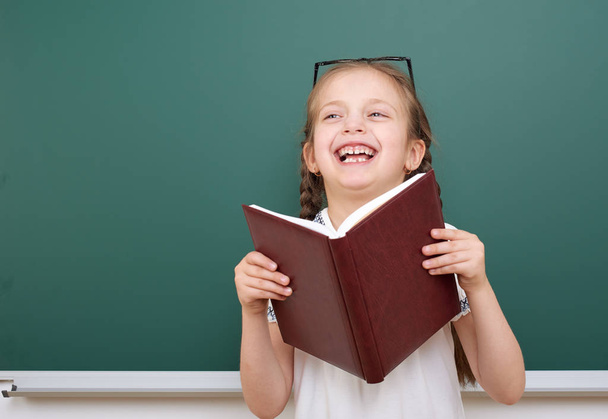 Шкільна дівчина читає книгу, позує на шкільній дошці, порожній простір, концепція освіти
 - Фото, зображення